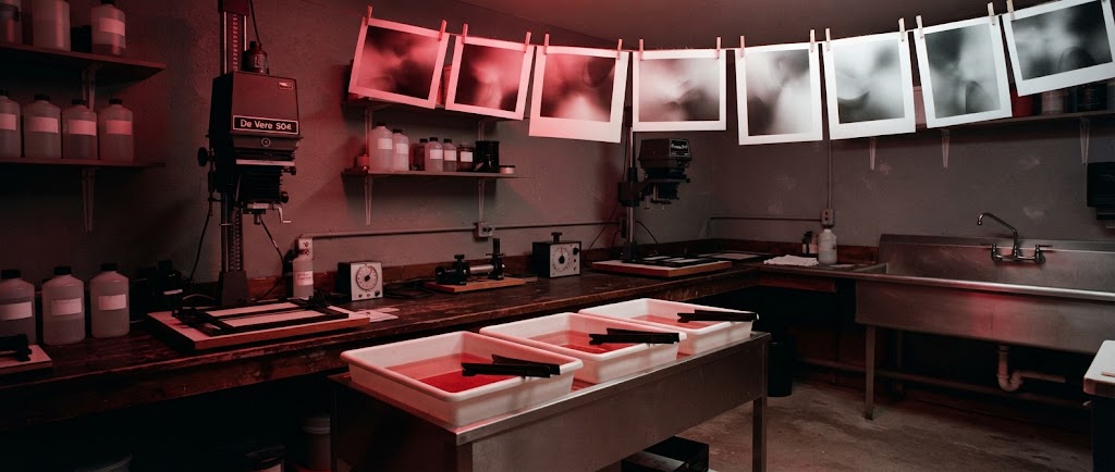 Artist's impression of the planned darkroom in red safelight: two enlargers, developing trays and prints hanging on a line